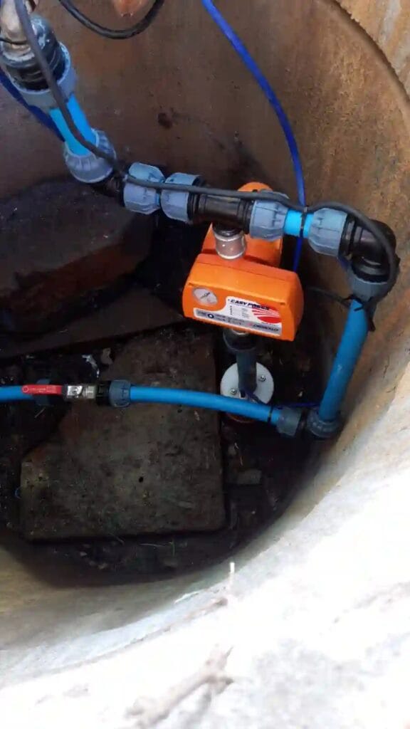 Automat sterujący Pedrollo EASY PRESS (pomarańczowy) zainstalowany na głowicy studni głębinowej (w kręgach), jako sterownik systemu nawadniania.