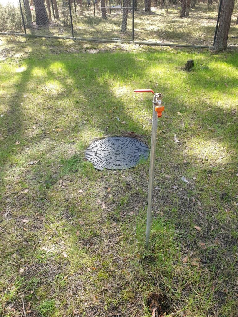 Kran ogrodowy (punkt czerpalny) zainstalowany na stalowym słupku przy włazie do komory rewizyjnej studni głębinowej.