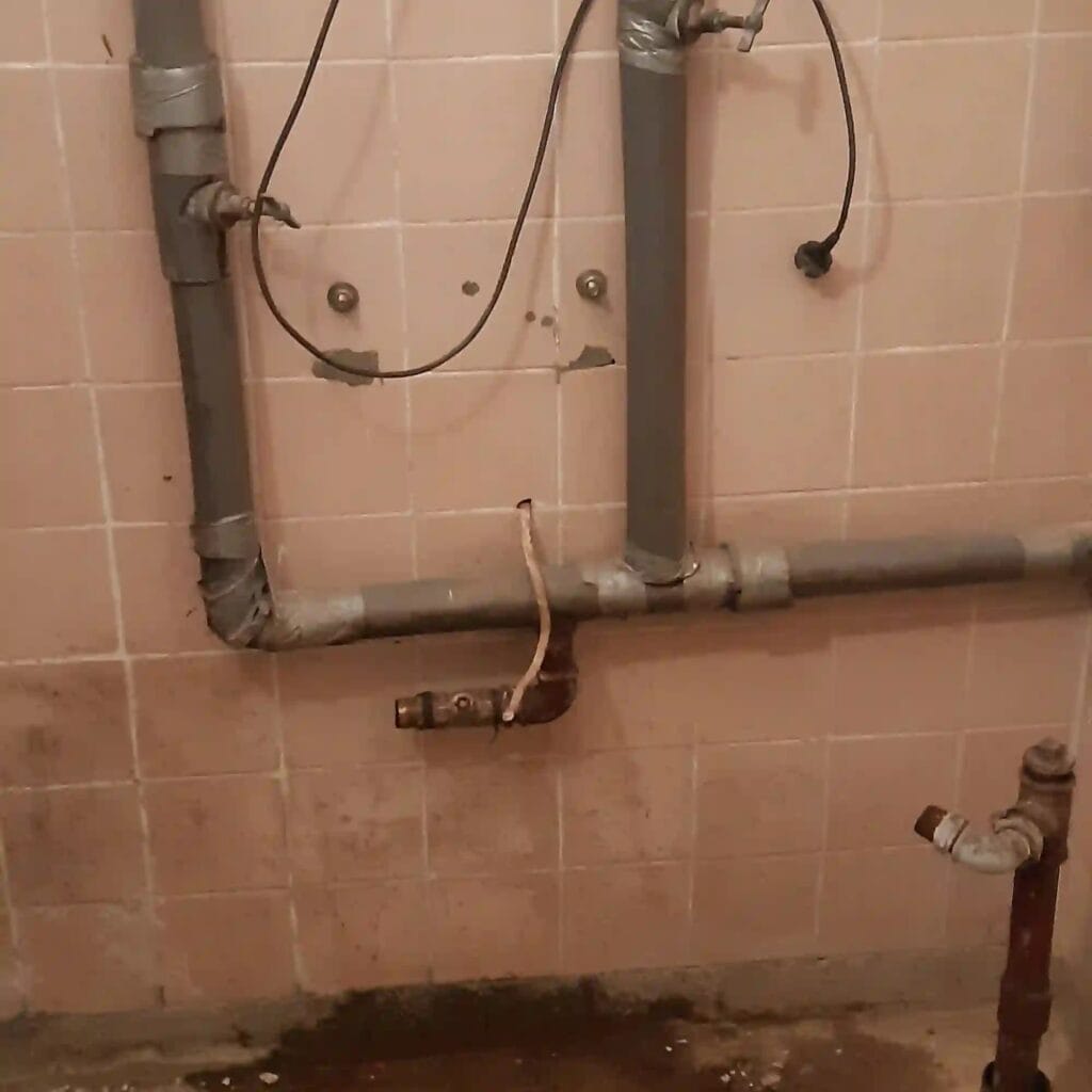 Krytycznie nieszczelna i zaniedbana instalacja hydrauliczna, z rurami PP prowizorycznie "naprawionymi" za pomocą srebrnej taśmy klejącej.