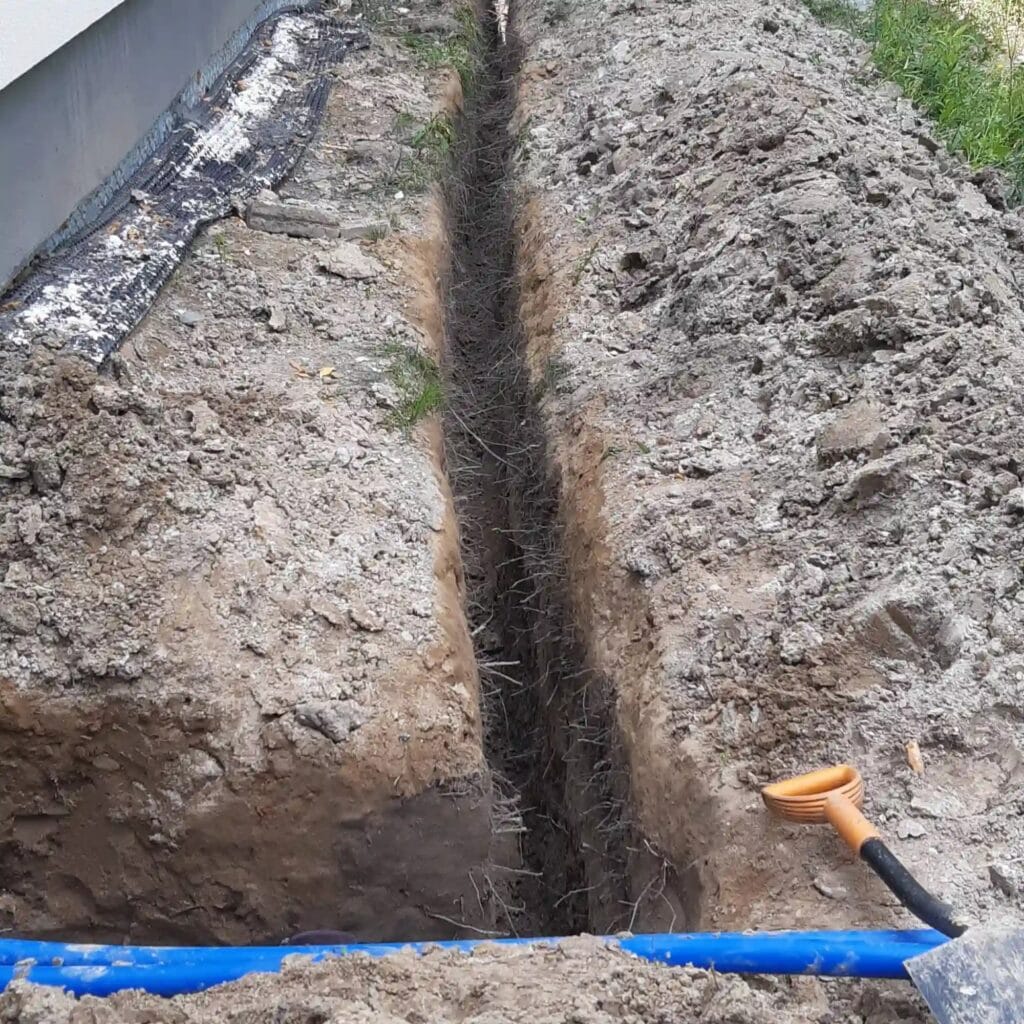 Niebieska "arteria" wodna (rura PE) ułożona na dnie głębokiego, precyzyjnego wykopu w trudnym, pełnym korzeni gruncie.