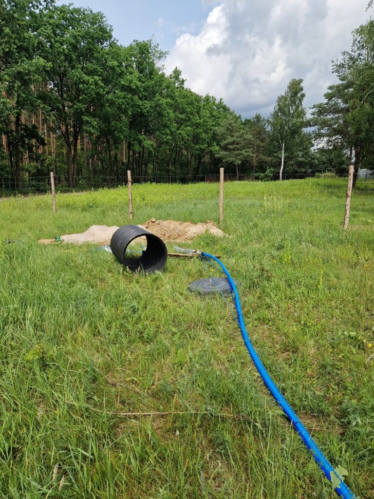 Początkowy etap montażu studni: rura PE z odwiertu oraz elementy obudowy (rura karbowana i właz) przygotowane do montażu suchej komory rewizyjnej.