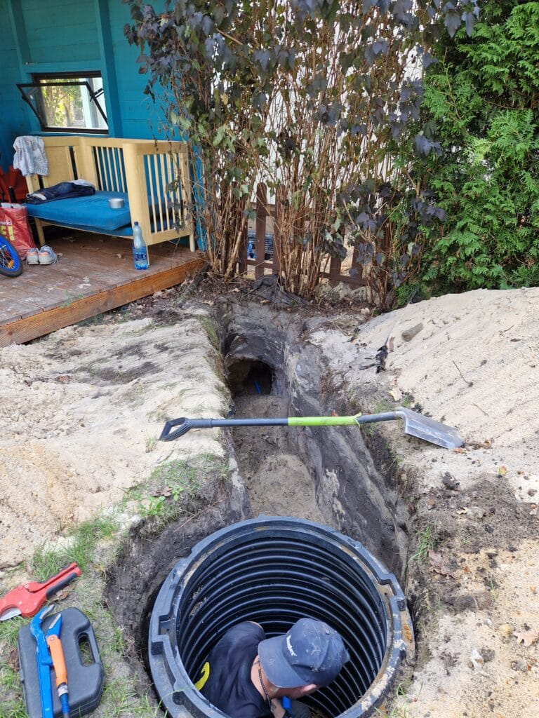 Instalator Hydromonters.pl pracuje wewnątrz suchej obudowy studni (rury karbowanej), wykonując przyłącze wodne w głębokim wykopie poniżej strefy przemarzania.