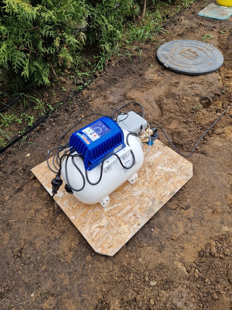 Zestaw hydroforowy z niebieskim falownikiem (inwerterem Pedrollo EasyPed Pro) i białym zbiornikiem przeponowym, ustawiony na płycie OSB obok włazu do studni.