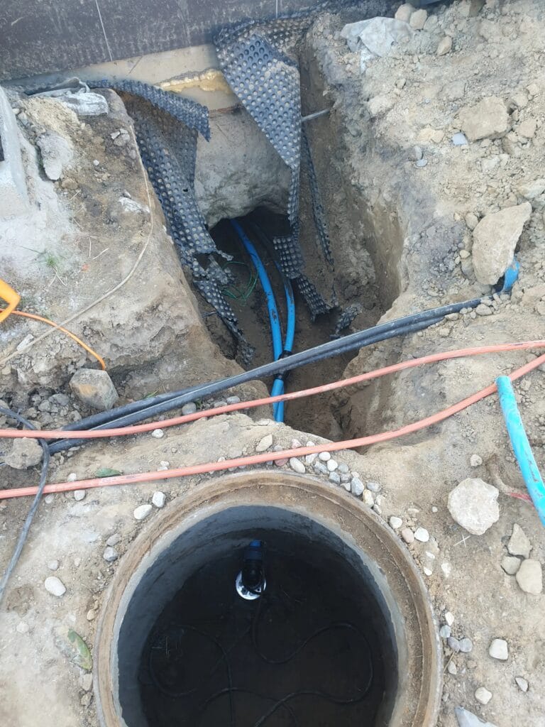 Kompleksowe przyłącze mediów Hydromonters.pl: rury wodne PE i rury osłonowe (peszle) na kable, prowadzone w jednym wykopie od studni do fundamentu.