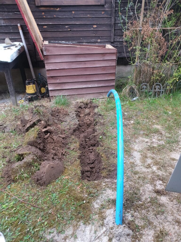 Niebieska pompa ręczna (abisynka) zainstalowana w ogrodzie, służąca jako awaryjne lub ogrodowe ujęcie wody.