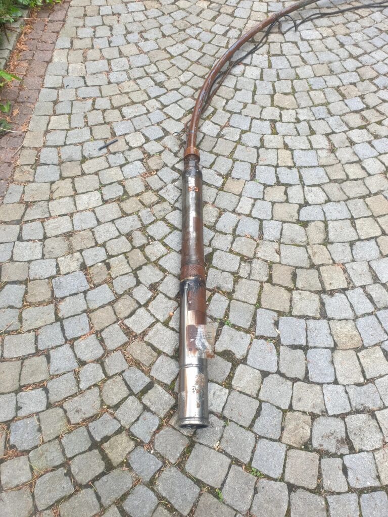 Zniszczona pompa głębinowa wyciągnięta ze studni, cała pokryta grubym, rdzawym osadem (bakterie żelaza) z powodu zażelazionej wody.