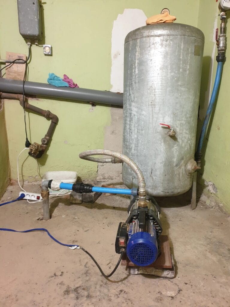 Stara, nieprawidłowa instalacja hydroforowa z pompą powierzchniową i skorodowanym zbiornikiem ocynkowanym, wymagająca pilnej modernizacji.