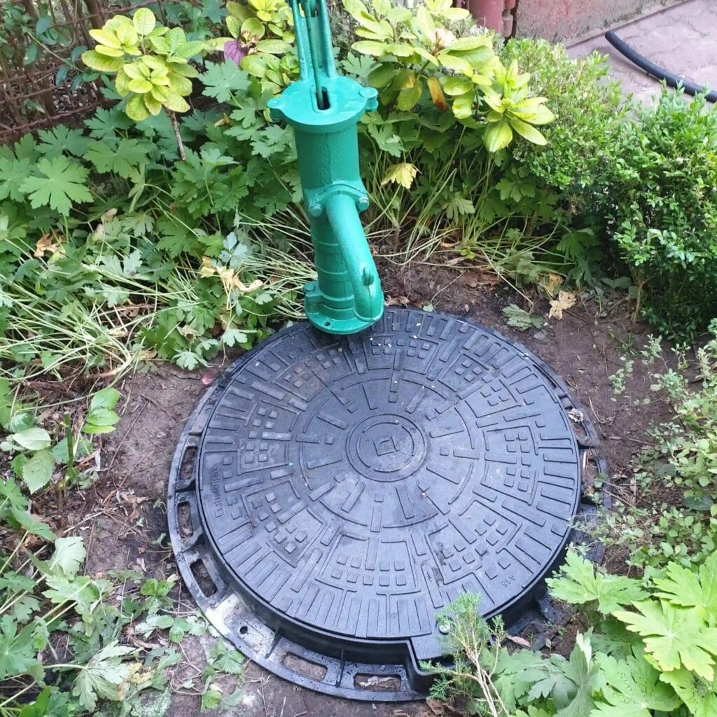 Zielona pompa ręczna ("abisynka") obok włazu do studni kręgowej, w której pracuje również pompa elektryczna.