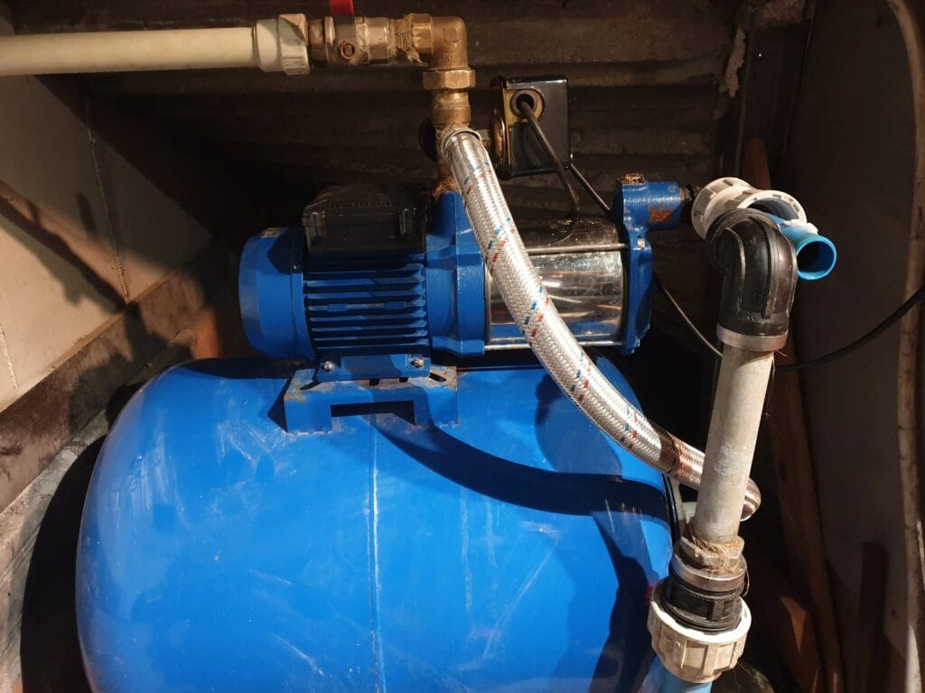 Zestaw hydroforowy (pompa i zbiornik) w komorze studziennej po awarii. Pompa jest odłączona, widoczne ślady uszkodzenia lub konieczności pilnej diagnostyki.