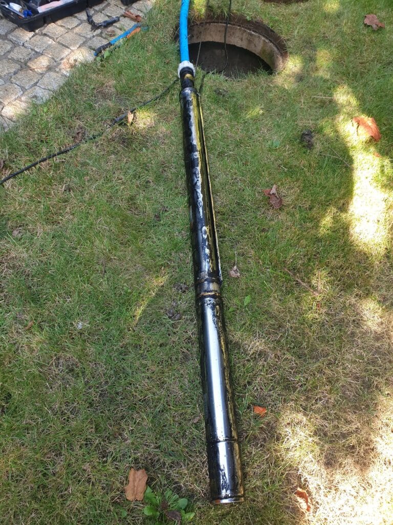 Wyczerpujący serwis pompy głębinowej w Warszawie; długa pompa wyciągnięta ze studni, pokryta intensywnym, czarnym osadem z manganu, świadczącym o problemach z jakością wody.
