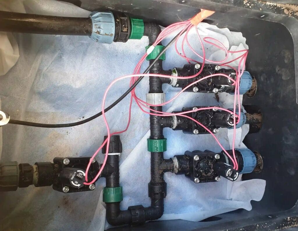 Montaż kolektora elektrozaworów (np. Hunter, Rain Bird) w skrzynce zaworowej. "Smaczek techniczny" to agrowłóknina (separator) pod spodem.