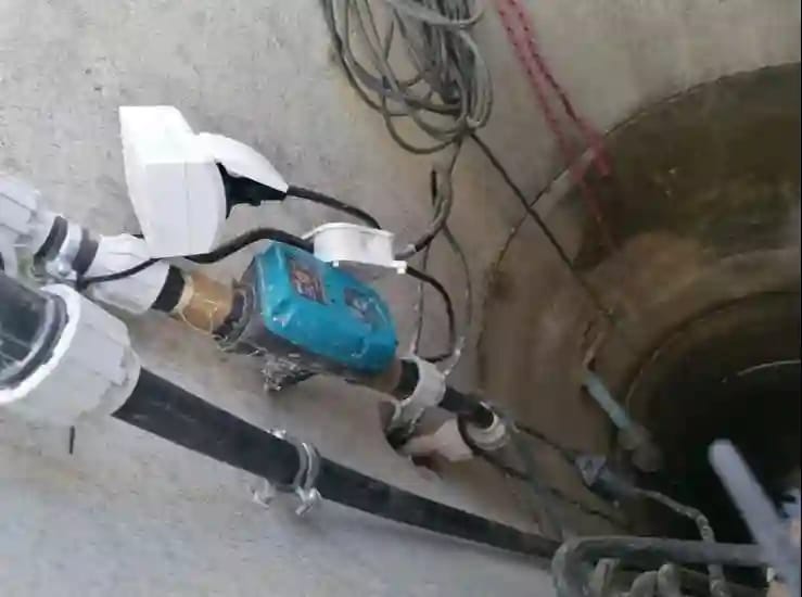 Amatorski montaż automatyki sterującej pompą wodną; widoczny niebieski automat ciśnieniowy (sterownik) typu PC-59 podłączony do rur PE w komorze studni kręgowej.