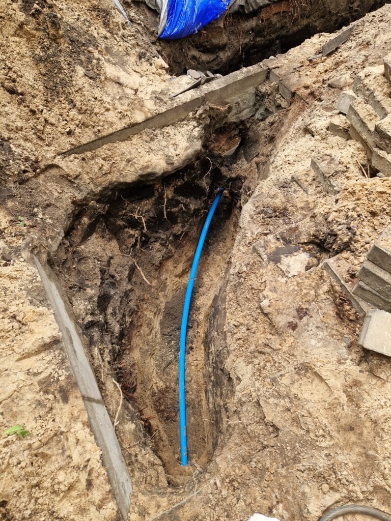 Precyzyjny, głęboki wykop "chirurgiczny" pod rurę PE, wykonany ręcznie tuż obok istniejących fundamentów (płyt betonowych).