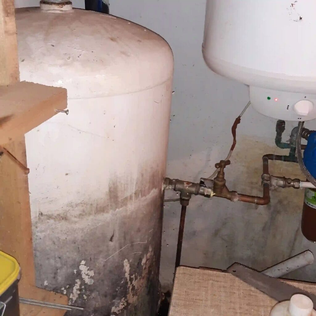 Masakryczny stan zbiornika hydroforowego: widoczna zaawansowana korozja i zagrzybienie na dnie zbiornika w wilgotnej piwnicy.