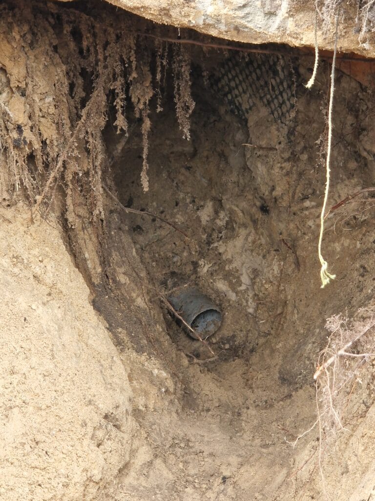 Serwis awaryjny Hydromonters.pl: głęboki wykop diagnostyczny odsłania stary, betonowy przepust (rurę osłonową) w fundamencie.