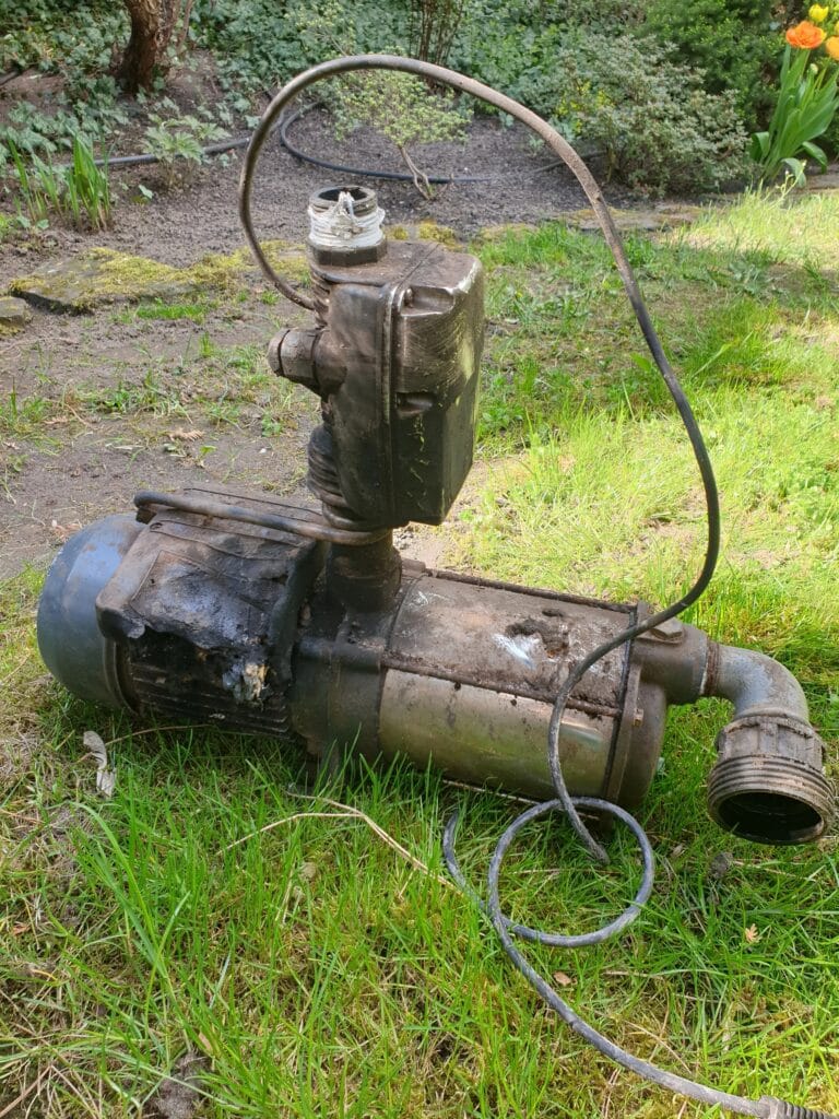 Spalona pompa hydroforowa typu MHI 1300 z uszkodzonym automatem ciśnieniowym PC-15 (wyłącznikiem), leżąca na trawie. Obraz ilustrujący skutki pracy na sucho (bez wody) lub zwarcia.