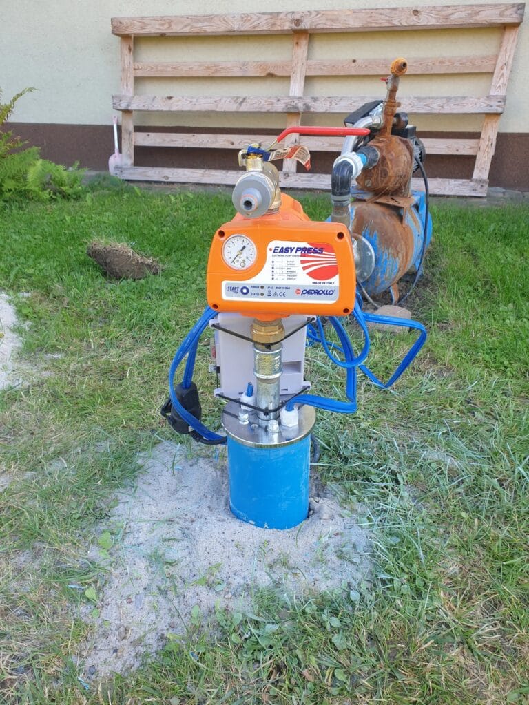 Modernizacja ujęcia: Nowy automat Pedrollo EASY PRESS (pomarańczowy) zastępuje starą, rdzewiejącą pompę hydroforową (w tle).