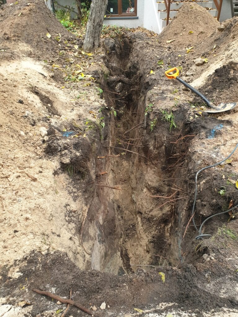 Efekt ciężkiej pracy ręcznej: głęboki, precyzyjny wykop pod przyłącze wodne, wykonany ręcznie w trudnych warunkach gruntowych.