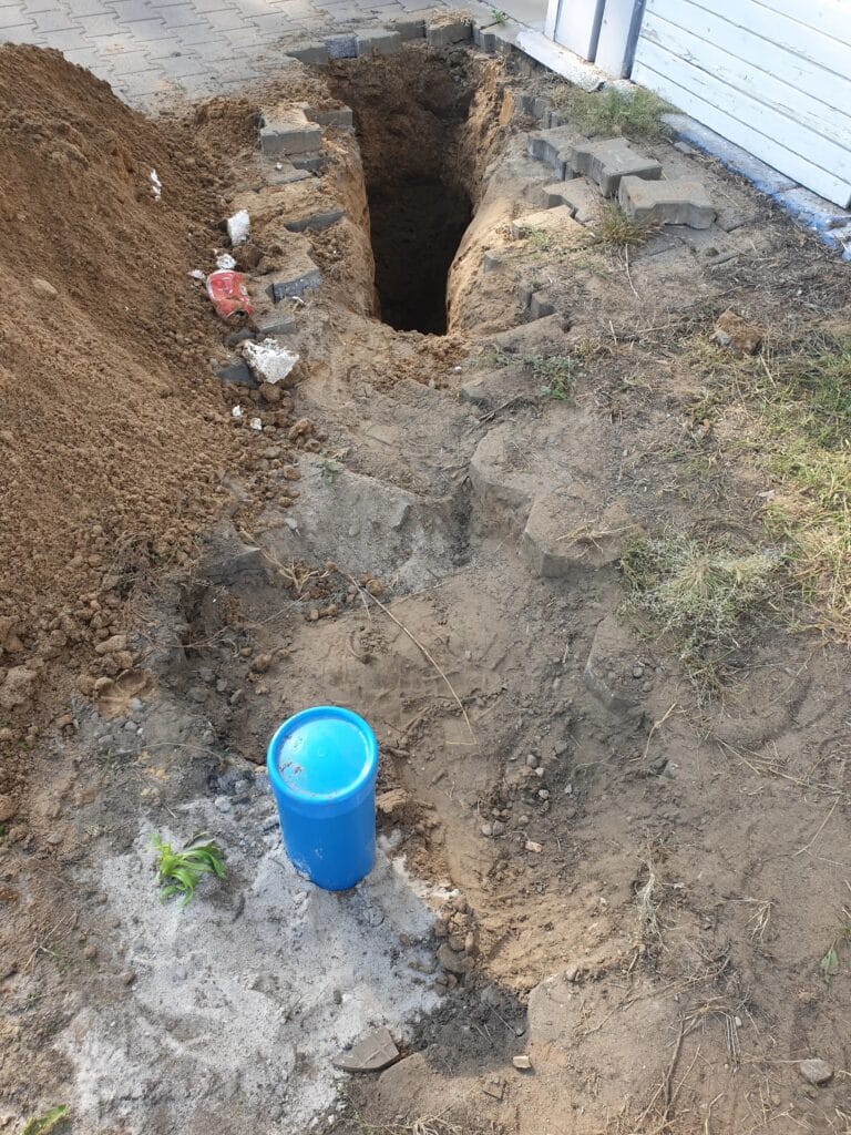 Odkopana hermetyczna głowica studni głębinowej (niebieska) i start głębokiego wykopu (poniżej strefy przemarzania) pod przyłącze wodne do budynku.