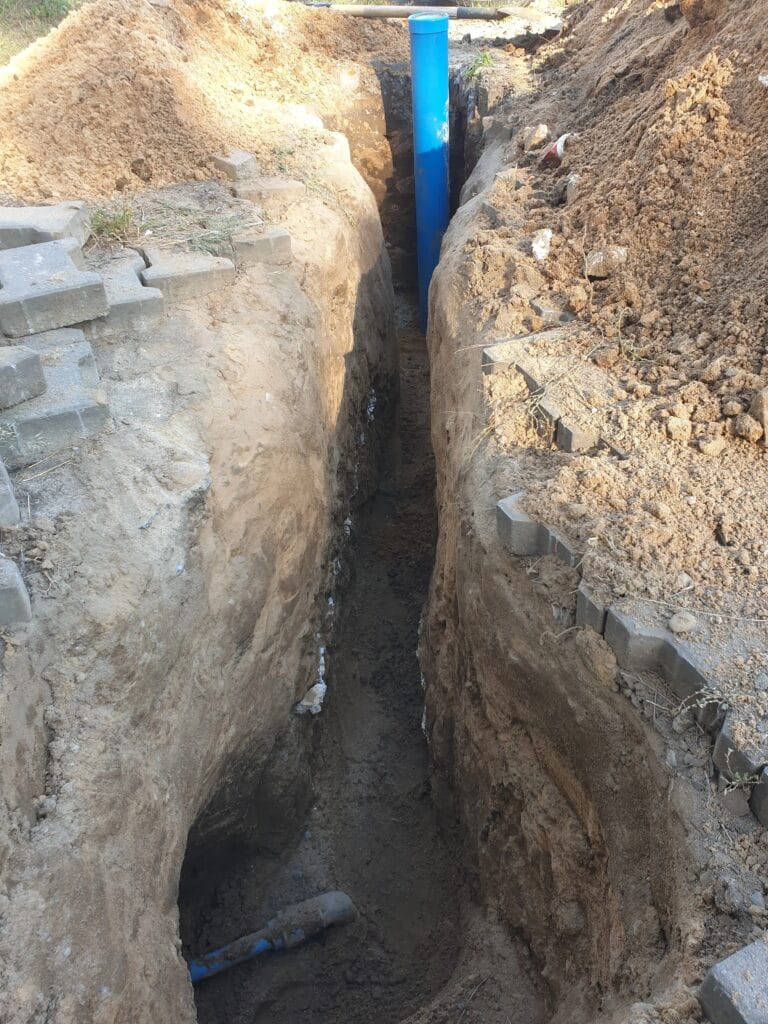 Głęboki, precyzyjny wykop (tranzyt) Hydromonters.pl, łączący rurę osłonową studni (góra) z przyłączem PE (dół), wykonany z poszanowaniem terenu (kostka brukowa).