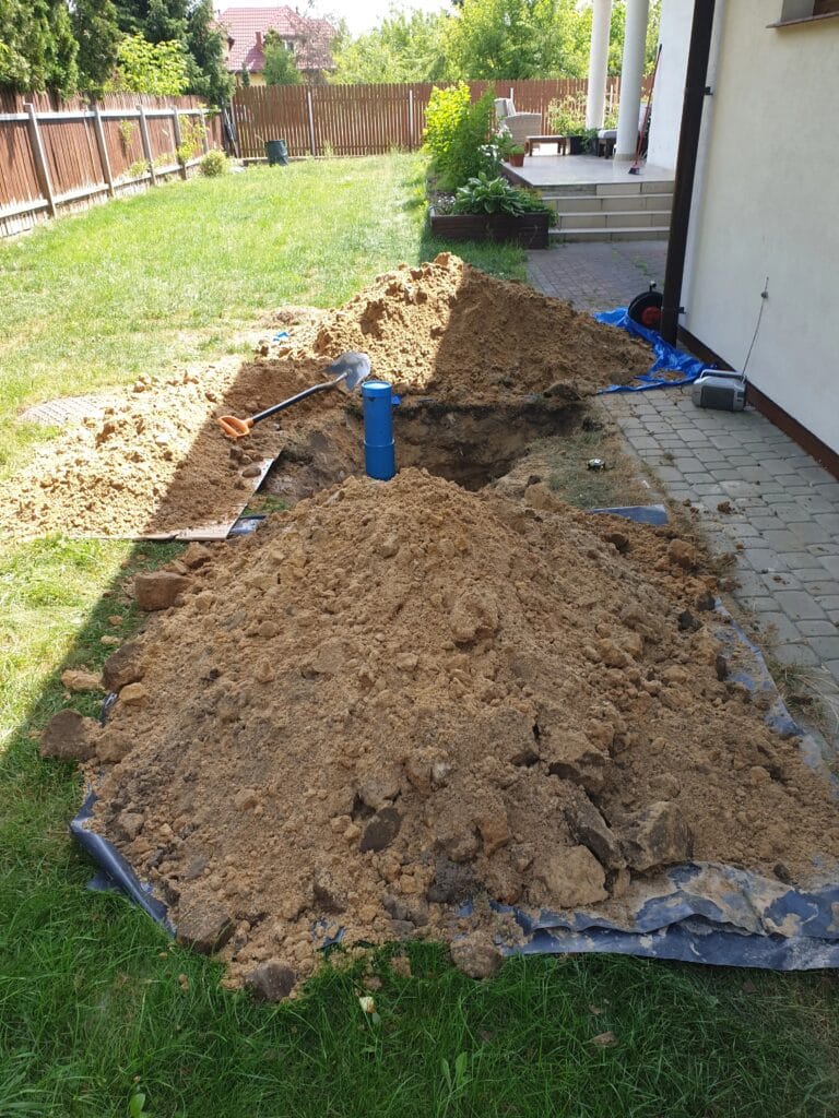 Wiercenie studni głębinowej (niebieska rura osłonowa) z precyzyjnym składowaniem urobku na plandekach w celu ochrony trawnika i ogrodu.