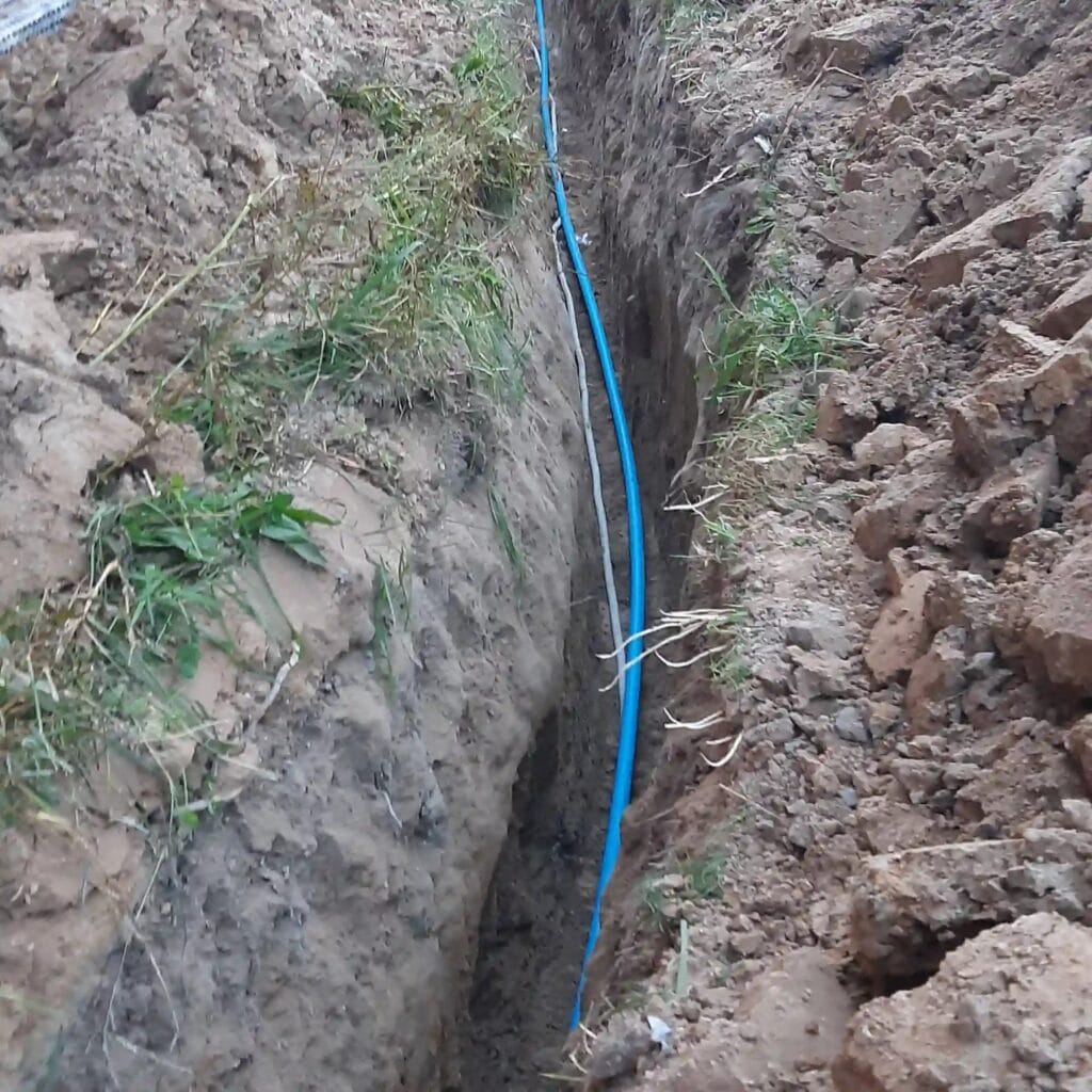 Układanie niebieskiej rury PE (przyłącza wodnego) w wykopie, łączącej studnię głębinową Hydromonters.pl z budynkiem.