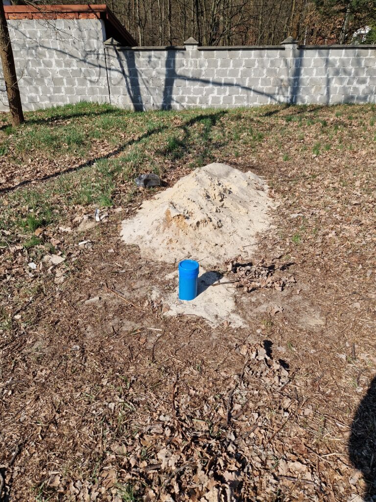 Zakończony odwiert studni głębinowej. Widoczna niebieska rura osłonowa (studzienna) i piasek (urobek) z wiercenia.