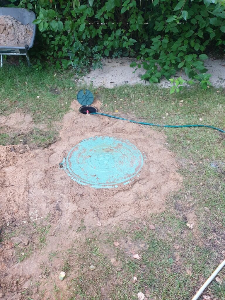 Zakończenie prac Hydromonters.pl (Białołęka): nowa obudowa studni głębinowej (mały, czarny właz) obok starej, betonowej studni kręgowej (duży, turkusowy właz).