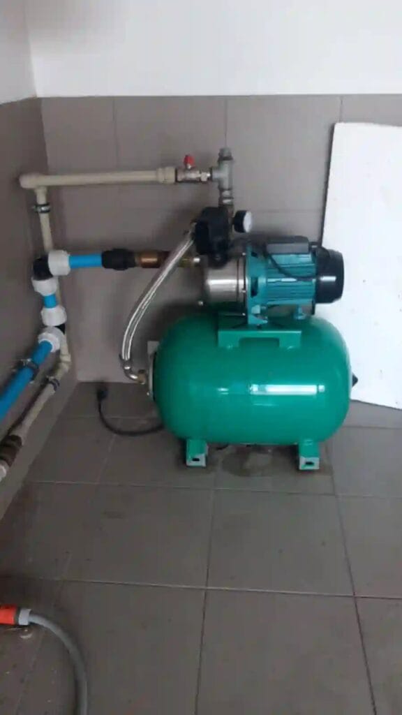 Prawidłowy montaż zestawu hydroforowego (pompa JY-1000 i zbiornik) w suchej kotłowni, z widocznym wężem antywibracyjnym.