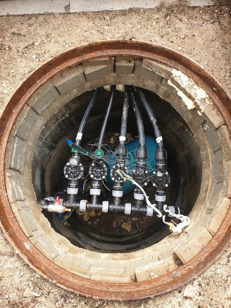 Kardynalny błąd: kolektor elektrozaworów systemu nawadniania i zbiornik przeponowy (niebieski), zainstalowane w głębokiej, betonowej komorze studziennej.